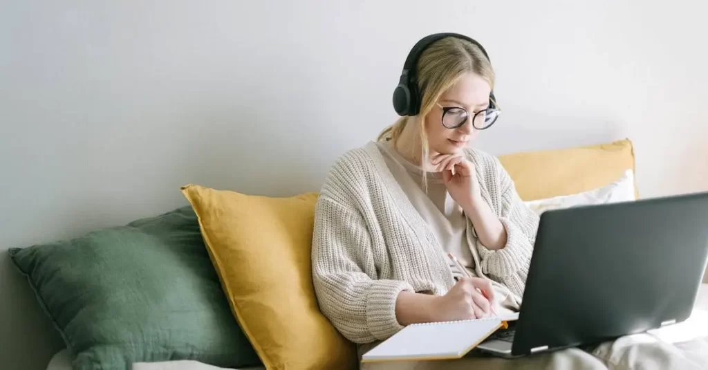 A woman is enjoying the benefits of webinars as she sits on a couch with headphones and a laptop.
