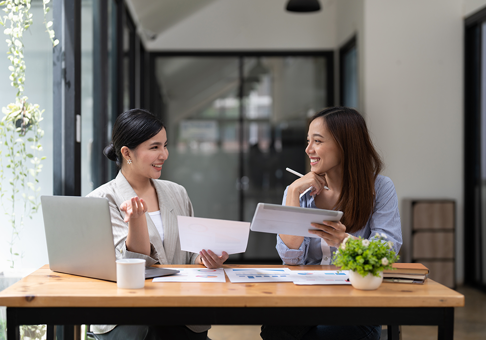Two women engaging in Account-Based Marketing (ABM), sitting at a table and attentively reviewing papers.