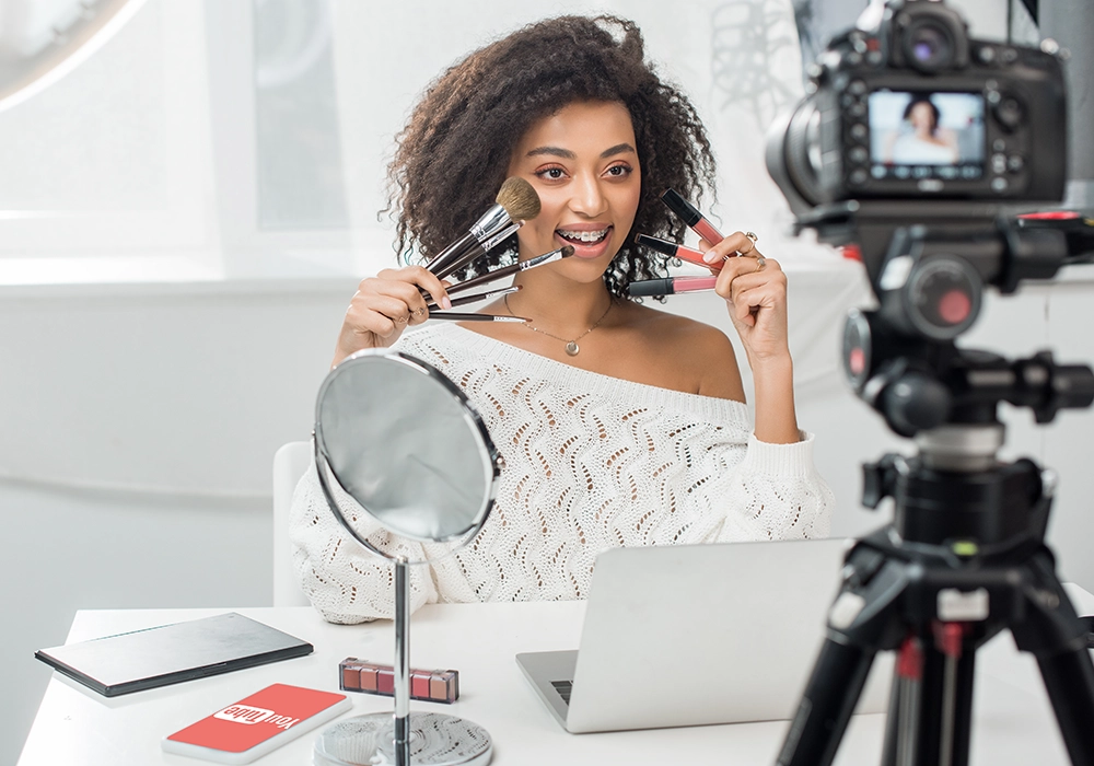 A Social Media Influencer in front of a video camera with makeup on her face.
