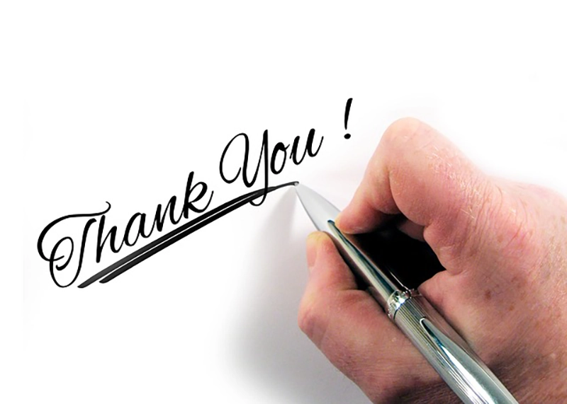 A hand expressing gratitude by writing the word thank you on a piece of paper.