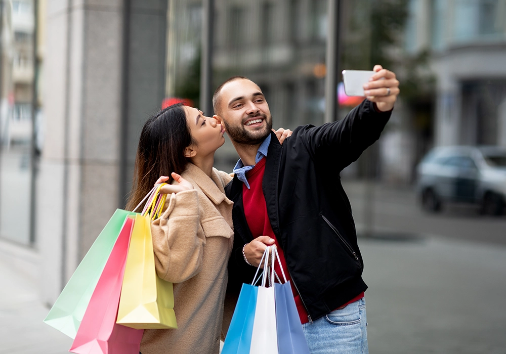 A man and woman documenting their purchase decisions with a selfie and shopping bags.