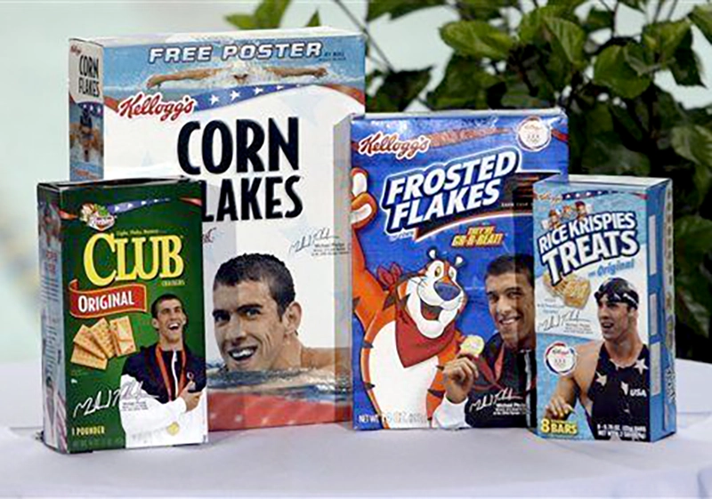Variety of Kellogg's cereal boxes including corn flakes, club original, frosted flakes with celebrity endorsements gone wrong, and rice krispies treats displayed on a table.