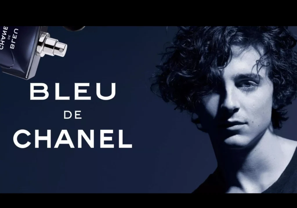 Advertisement for bleu de chanel featuring the power of celebrity with Timothee Chalamet with curly hair and a small perfume bottle against a dark background.