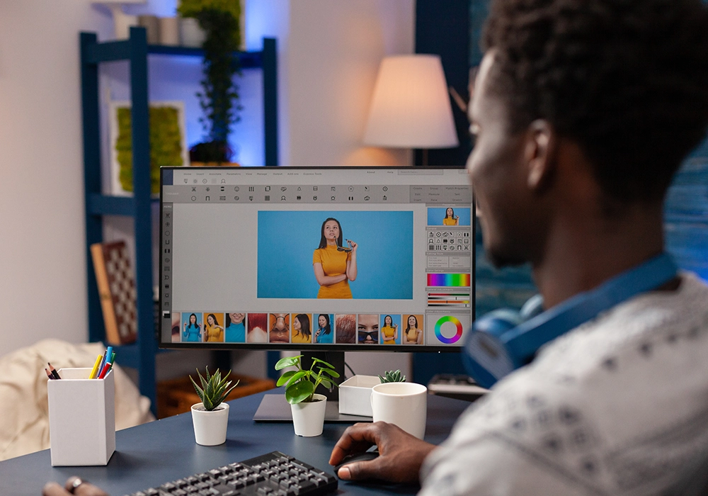 A man editing a photo of a woman for Facebook ads on a computer screen in a well-lit home office.