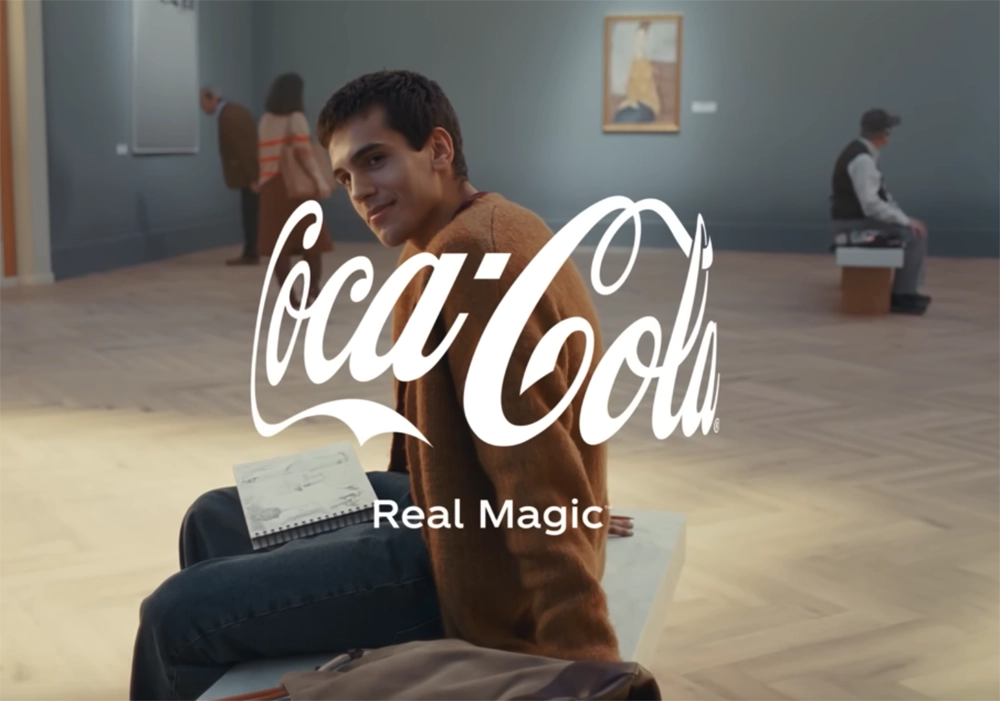 A young man sitting on a museum floor, sketching, while a Coca-Cola Campaigns logo with the slogan "real magic" overlays the image.
