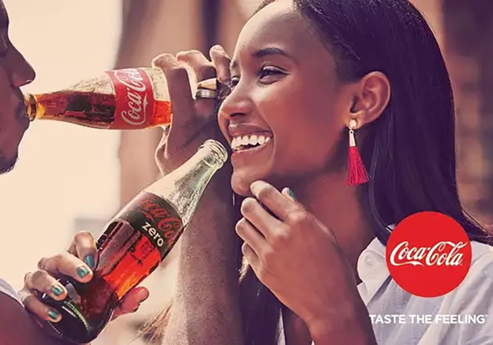 A man and a woman share a joyful moment while participating in Coca-Cola Campaigns, drinking Coca-Cola and Coca-Cola Zero from glass bottles.