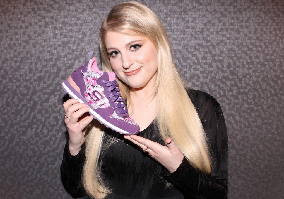 Megan with long blonde hair holding a purple sneaker from a celebrity partnership with a graphic design, smiling at the camera.