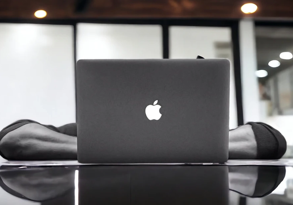 A person relaxes in a modern workspace, feet propped on the table, behind a laptop with an Apple logo. It seems like even in everyday settings, Apple's celebrity endorsements extend their iconic appeal.