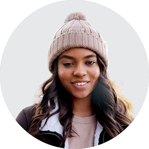 Emily wearing a beige beanie and a brown jacket smiles gently against a light grey background.