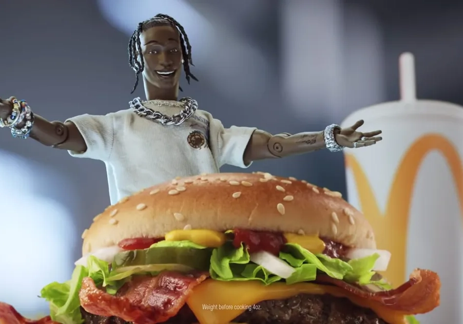 Travis Scott, with braided hair, holds out its arms behind a large hamburger with toppings and a paper cup with a McDonald's logo, reminiscent of celebrity food endorsements.