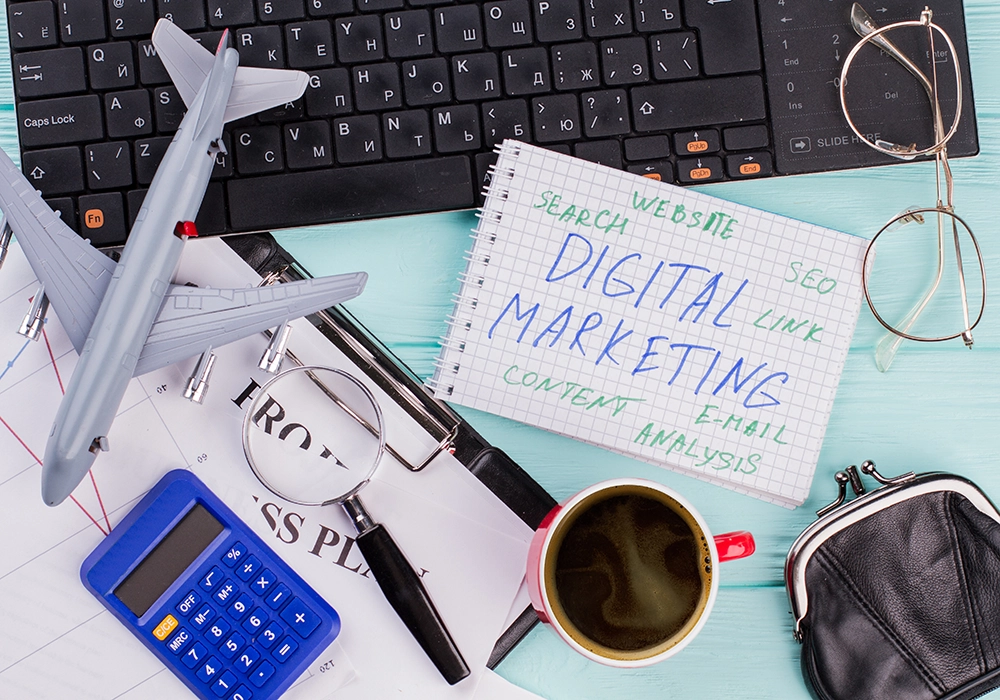 Desk with keyboard, eyeglasses, plane model, magnifying glass, calculator, coffee, and a notepad reading "DIGITAL MARKETING SIDE HUSTLE" with related terms.