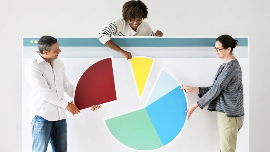 Three people stand behind a large pie chart graphic, each holding a different colored segment representing marketing performance indicators, and appear to be discussing or assembling the chart.