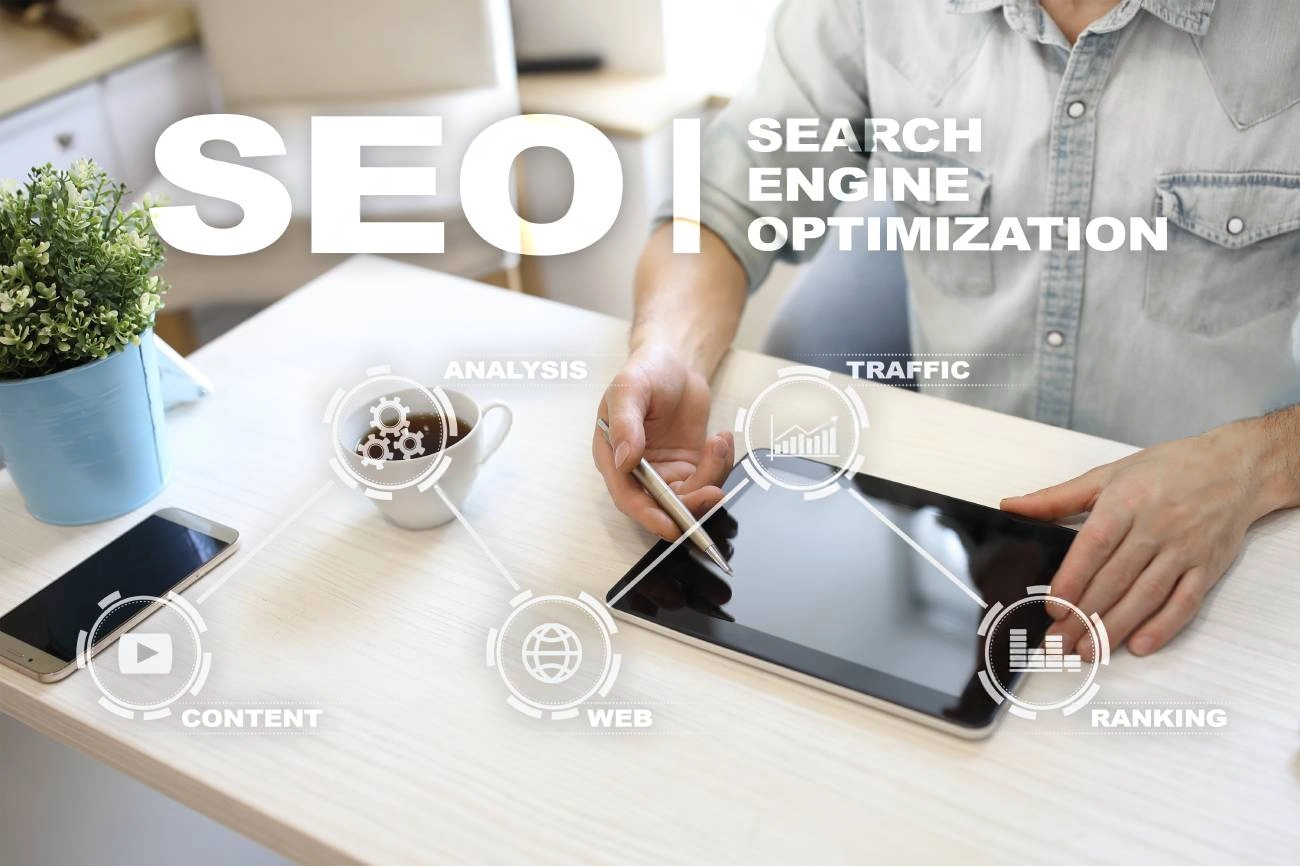 A person uses a tablet at a desk with a smartphone, plant, and coffee; digital icons and the words “SEO Search Engine Optimization” overlay the image, highlighting the importance of content writing tools for SEO.
