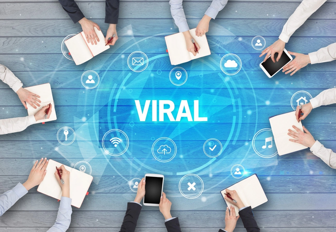 Businesspeople sit around a table with notebooks and tablets, brainstorming strategies on How to Create Viral Content, as a digital illustration displays the word "VIRAL" alongside various social media icons.
