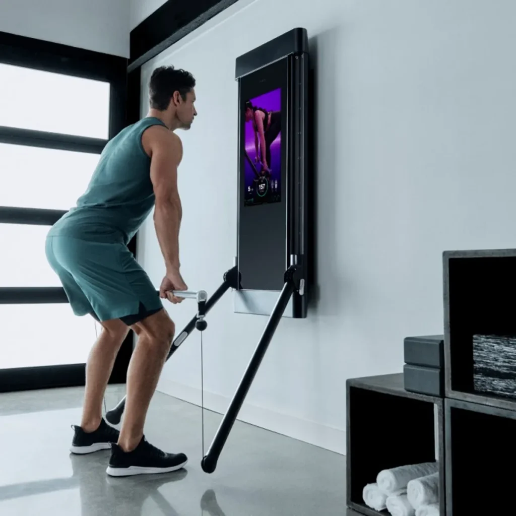 A man exercises with a wall-mounted smart fitness machine, following instructions displayed on the built-in screen, perfect for those curious about innovative workouts and seeking the latest in Tech Reviews.