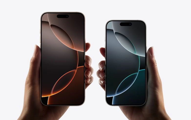 Two hands holding Apple iPhone 16 side by side; the left phone displays a warm-toned abstract wallpaper, while the right phone shows a cool-toned abstract wallpaper.