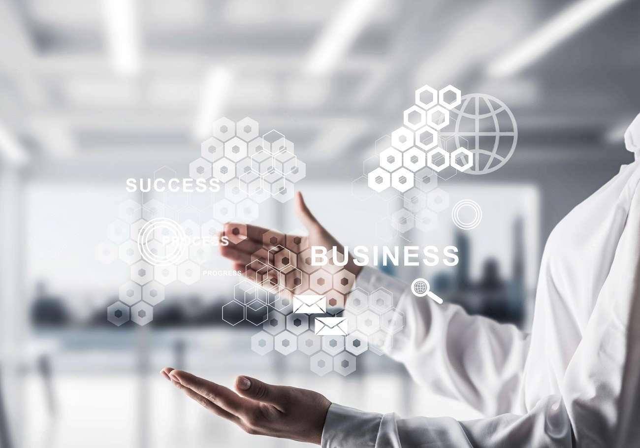 A person in a white shirt interacts with virtual hexagonal graphics labeled "Success" and "Business to Business Commerce" against a blurred modern office background.