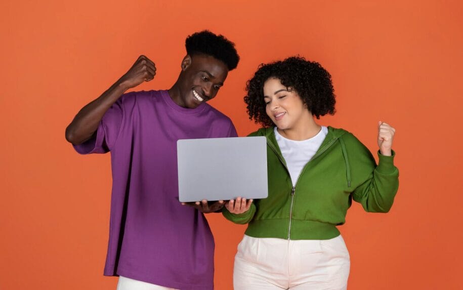 Two people stand against an orange background, holding a laptop and smiling with raised fists, celebrating as they complete a website credibility checklist.
